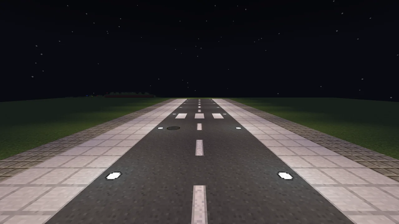 A roadway with a dashed center line and a crosswalk, sidewalks and stone paths either side, lit by roadway lights.
